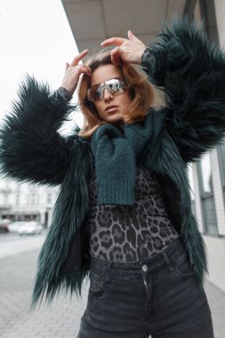 Havalı gözlüklü göz kamaştırıcı moda hanımı şehirde şık bir ceket ve süveter giyiyor.