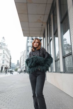 Şık, şık, şapkalı, leopar desenli tişörtlü ve tüylü ceketli güzel bir kız şehirde yürüyor.