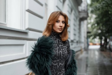 Güzel kızıl saçlı manken şehirde şık kıyafetler içinde yürüyüş yapıyor.