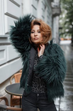 Şehirde poz veren, güzel, kızıl saçlı, moda elbiseli bir kadın.