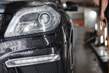 Araba yıkamada farları olan siyah bir SUV. Araba yıkama