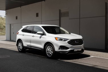 Güneşli bir günde şehrin yakınında beyaz bir SUV arabası.