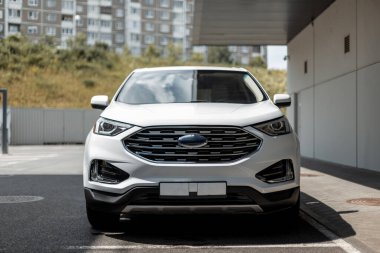 Güneşli bir günde şehrin yakınında beyaz bir SUV 'un önünde.