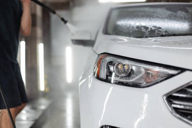 Adam arabasını yüksek basınçlı çamaşır makinesiyle yıkıyor. Oto yıkamada beyaz SUV.