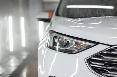 Farlı beyaz SUV arabası oto yıkamada yıkanıyor, yakın plan.