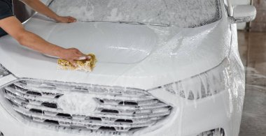 Adam araba yıkamada arabasını şampuan köpüğüyle yıkıyor. Araba bakımı