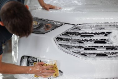 Süngeri olan bir erkek işçi araba yıkamada araba yıkar.