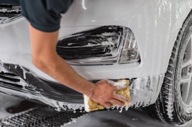 Süngerli bir işçi arabayı köpükle yıkar. Araba yıkama ve araba bakımı