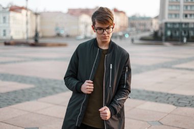 Moda siyah ceketli gözlüklü şık şehirli yakışıklı adam şehirde yürüyor.