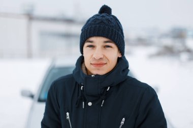 Karlı bir kış gününde moda ceketi giymiş örgü şapkalı yakışıklı bir adam. Erkek portresi