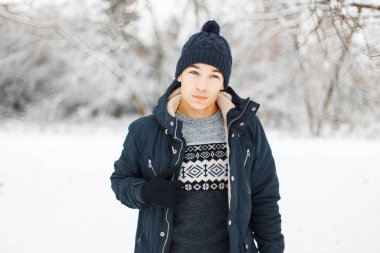 Süslü, yakışıklı, şapkalı, modaya uygun bir süveteri ve ceketi olan açık havada, karlı bir parkta eldivenli bir adam.