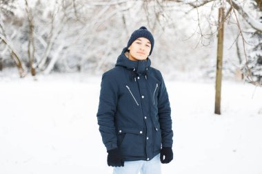 Klasik örgü şapkalı ve ceketli şık yakışıklı bir adam. Kışın karlı parkta yürüyor.