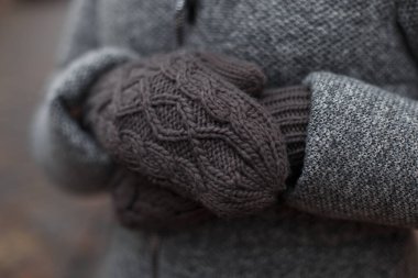 Female hands in vintage gray knitted mittens on a winter day outdoors clipart