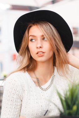 Moda yaz kıyafetleri içinde, şapkası ve örgü ören beyaz kazağı olan güzel bir kız model güneşli bir günde oturur ve dinlenir.