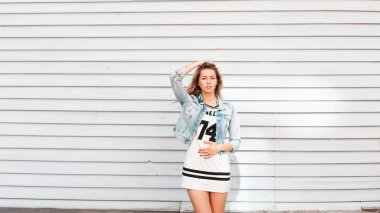 Kot ceketi ve elbisesi ile şık bir bahar kotu içinde güzel bir genç kız açık havada eski bir ahşap duvarın yanında duruyor.