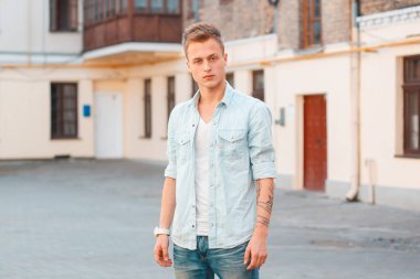 Moda kot gömlekli yakışıklı öğrenci sokakta dikilip kameraya bakıyor.