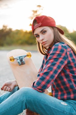 Güzel moda genç kız öğrenci modeli, çizgili gömlekli ve kot pantolonlu, güneş batarken parktaki asfaltta oturan. Güzel sokak kadını.