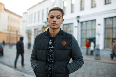 Moda desenli ceketli, modaya uygun genç erkek modeli şehir arka planında duruyor.