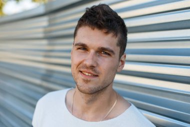 Caddedeki metal bir duvarın yanında şık kıyafetler içinde gülümseyen bir adamın mutlu ve yakışıklı portresi.