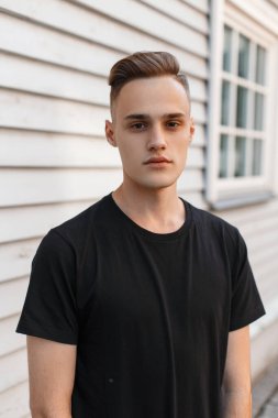 Moda modası geçmiş siyah tişörtlü şık bir Amerikan mankeni ahşap duvarın yanında duruyor.