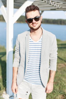 Moda kıyafetleri içinde, güneşli bir günde kumsalda güneş gözlüğü takan şık bir adam modeli.