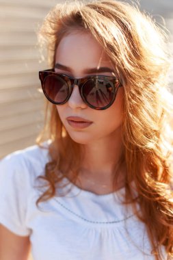 Gün batımında modaya uygun beyaz bir tişörtle şık güneş gözlüklü güzel bir kızıl saçlı kızın kadın portresi.