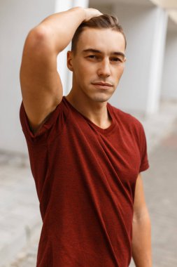 Şehirdeki kırmızı tişörtlü, saçları düzleştirilmiş, saç stili olan yakışıklı bir genç.