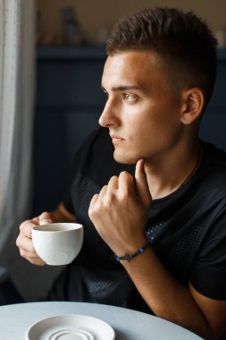 Yakışıklı genç adam oturuyor ve aromatik kahve içiyor.