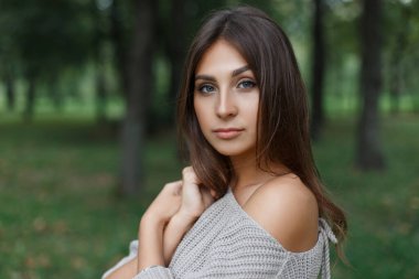Parkta yeşil doğayla ilgili bir süveter giyen genç ve güzel bir manken.
