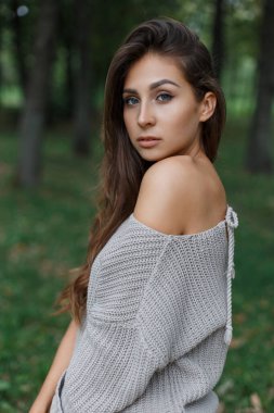 Parkta yeşil bir arka planda yürüyen, temiz ciltli, moda örgü süveterli, genç ve güzel bir kadın.
