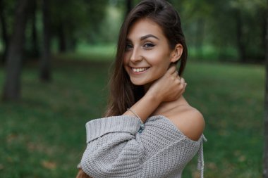 Doğada bir parkta moda örgüsü süveter giyen mutlu, güzel, yeni model bir kız.