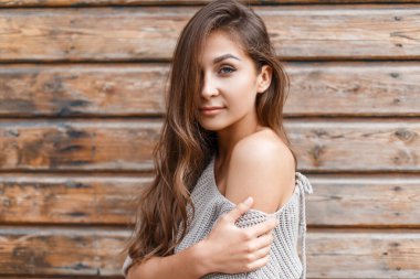 Ahşap bir duvarın arkasında örülmüş bir süveter içinde berrak cilt yüzlü güzel bir kız.