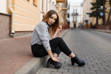 Şık, güzel, hippi kız, burnu delikli, çizmeli, kot pantolonlu, moda tişörtlü şehirde oturuyor.