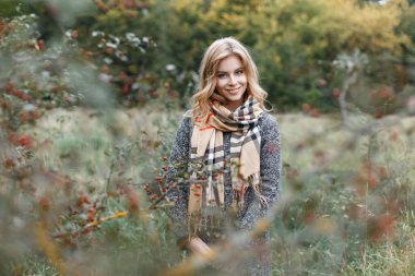 Doğada sonbahar ormanlarında yürürken atkı takmış, gülümseyen genç ve mutlu bir kadın.