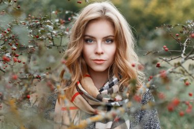 Genç ve güzel bir kadın ormanda duruyor, doğada böğürtlenlerle dolu bir ağacın yanında.