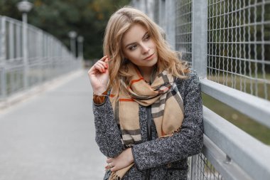 Şık bir sonbahar paltosu giymiş atkısı olan genç ve güzel bir kadın sokakta yürüyor.