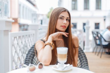 Yazın güzel bir kız açık bir kafede oturur ve güneşli bir günde kahve içer.