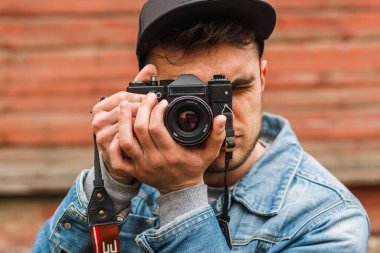 Havalı kot elbiseli yakışıklı hippi fotoğrafçı klasik bir kamerayla fotoğraf çekiyor.