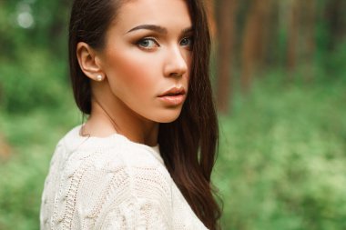 Doğal bir kadın portresi. Temiz bir yüzü olan, örgü ören genç bir kadın. Ormanda yeşil bir arka planda.