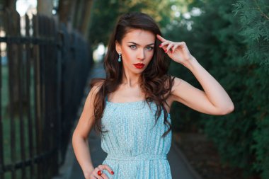 Parkta yürüyen, kırmızı dudaklı, modaya uygun elbisesi olan genç ve güzel bir bayan.