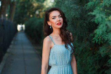 Uzun turkuaz elbiseli zarif genç bayan parkta yürüyor.