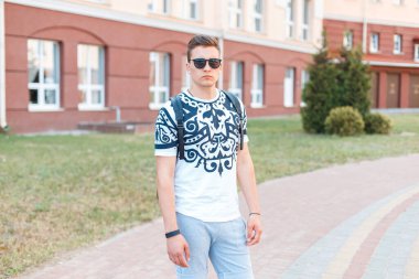 Tişörtlü, güneş gözlüklü ve sırtında sırt çantası olan yakışıklı bir delikanlı sokakta yürüyor.