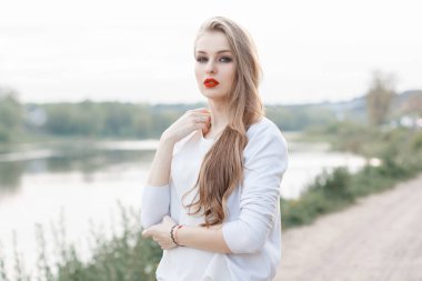 Güzel, modaya uygun, kırmızı dudaklı, beyaz süveterli kız mankeni sahilde yürüyor.