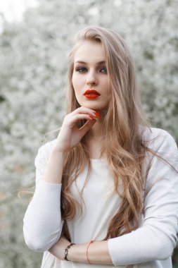 Doğada çiçek açan bir ağacın yanında beyaz süveter içinde güzel bir genç kız.