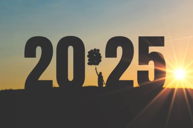 Mutlu kız balon tutuyor ve 2025 yılının gün batımında bir tarlada sayılarla duruyor. Yeni yıl ve hayaller 2025