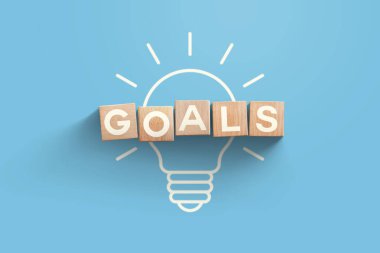 Hedefler, yaratıcı fikirler. Mavi zemin üzerinde tahta bloklardan yapılmış hedeflerle parlayan ampulün üst görüntüsü, hedef belirleme kavramı. Başarı, Yaratıcı Fikir. İş ve Geliştirme. Açılış