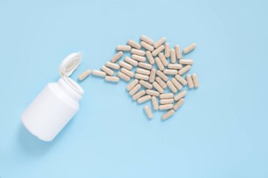 Plastik kaplardan besin takviyesi kapsülleri dökülüyor. Mavi arkaplan ve minimum stil. İlaç, sağlık hizmeti veya vitamin teması.