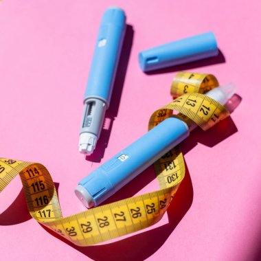 Mavi Ozempic kalemler ve parlak pembe masadaki bant. Sağlık, sağlık ve tıbbi yardımın soyut bir temsili. Enjektörlerin etrafındaki sarı şerit..