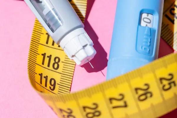 Pembe yüzeye dizilmiş Ozempic insülin kalemleri. Sağlık, endokrinoloji ve yaşam tarzı tıp konsepti. Enjektörlerin etrafındaki sarı şerit..