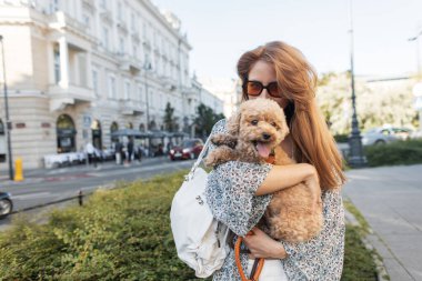 Kendine güvenen genç bir kadın köpeğini canlı bir şehirde tutuyor. Gülümseyen ve kaygısız, evcil hayvan arkadaşlığının ve modern sokak modasının özünü yakalıyor..